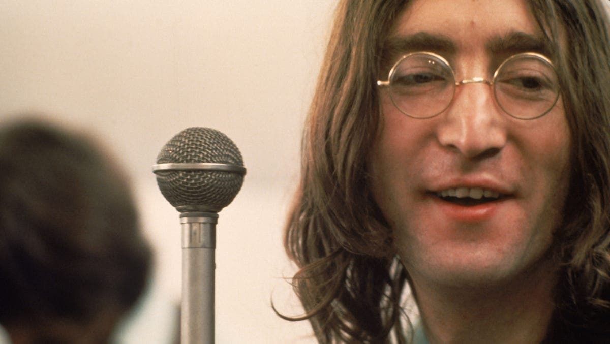 Close-up of a man with long hair and glasses beside a microphone, smiling slightly