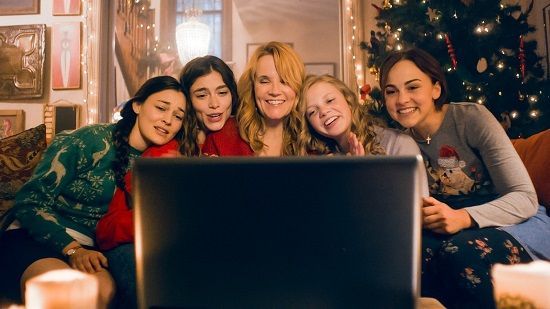 Five people, faces lit by a laptop screen, on a sofa in a decorated room, celebrating Christmas.