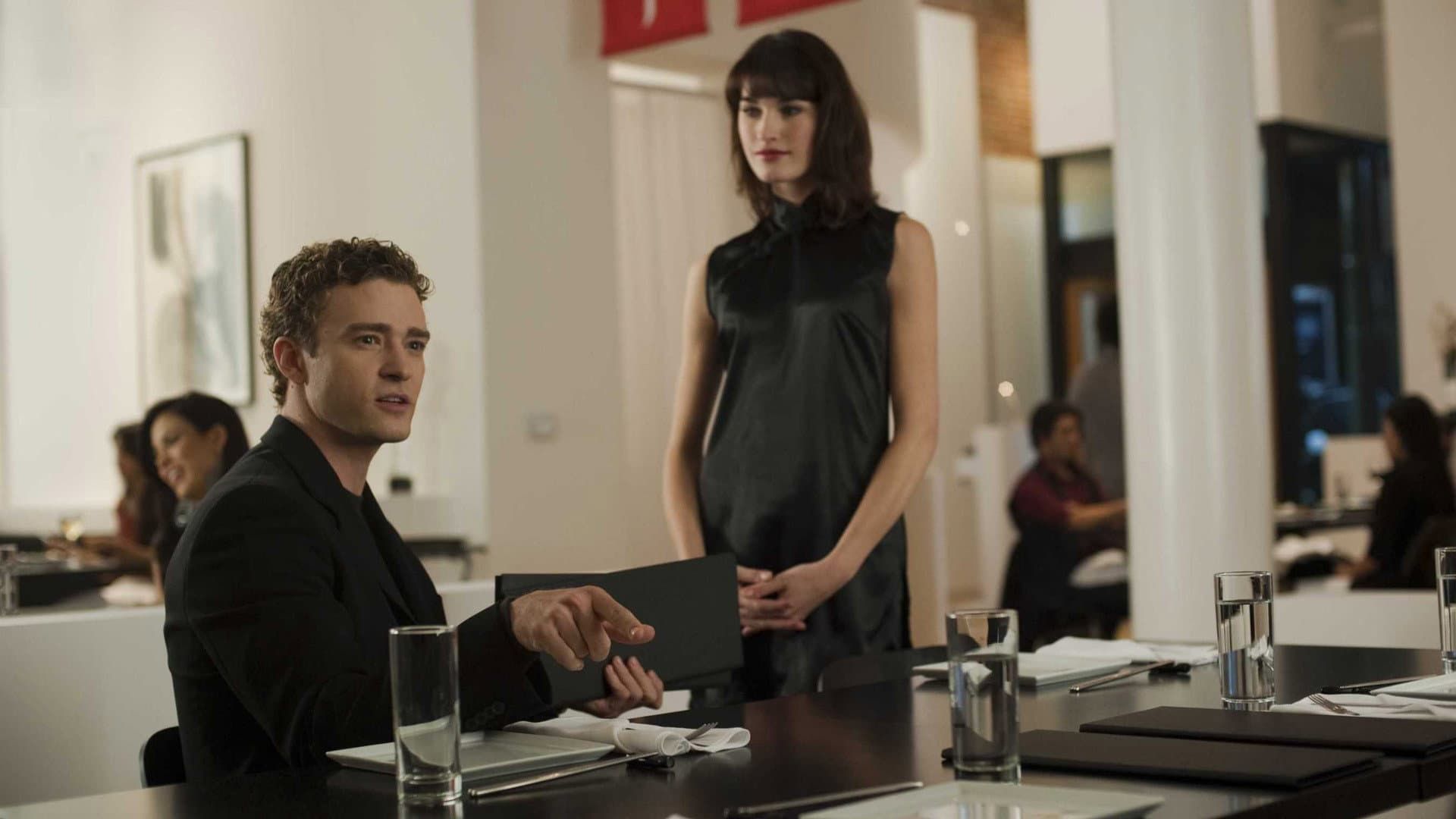 Two people at a restaurant table, one seated with a laptop and one standing nearby.