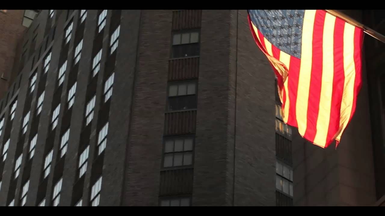 American flag waving in front of a tall brick building with many windows.