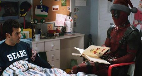 Deadpool reads a book to a man in a Bears sweatshirt, seated beside him in a bedroom.