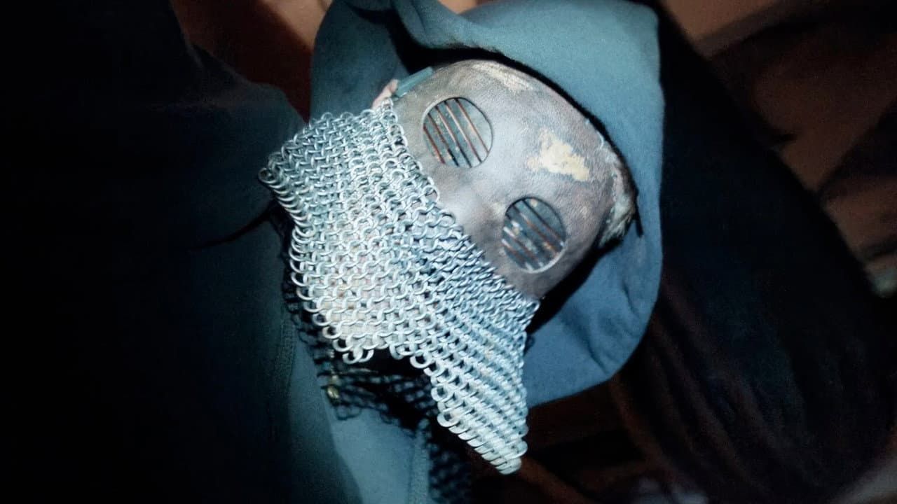 A small silver robot figurine with mesh around its face, held in a blue-gloved hand