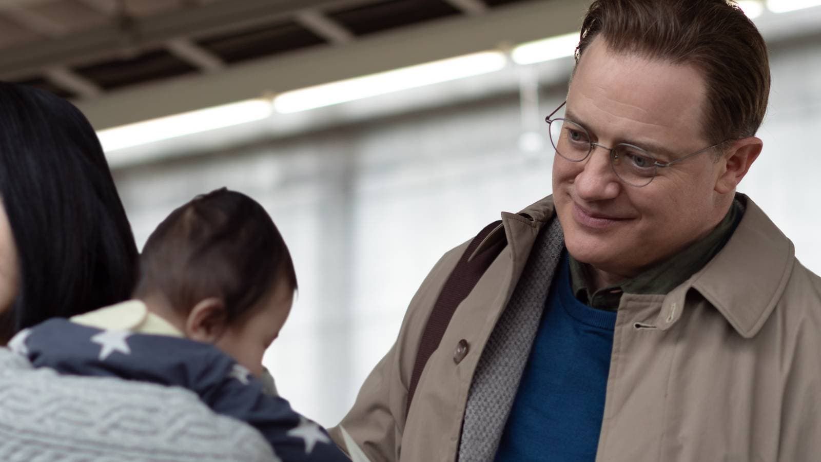 Man in a tan coat smiles beside a child in a subway or train station.