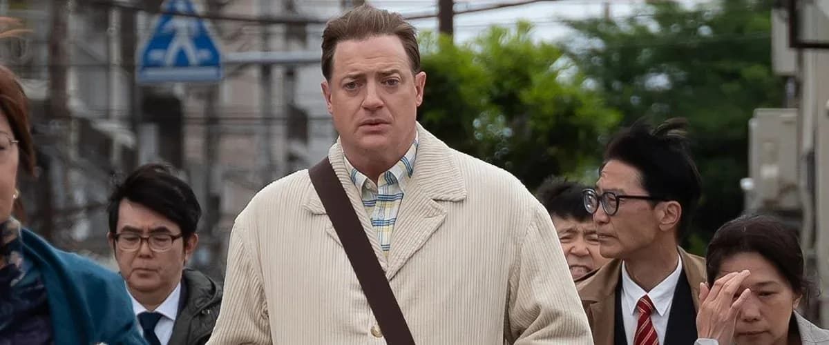 Brendan Fraser walks through a city street, surrounded by people in business attire.