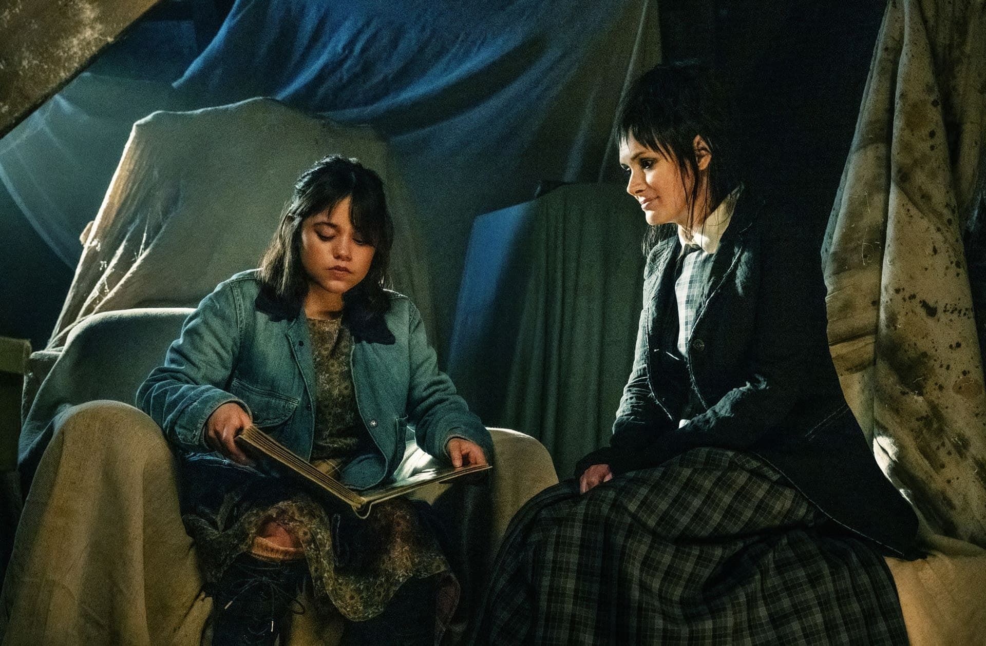 Two people sit inside a tent, reading together under dim light.