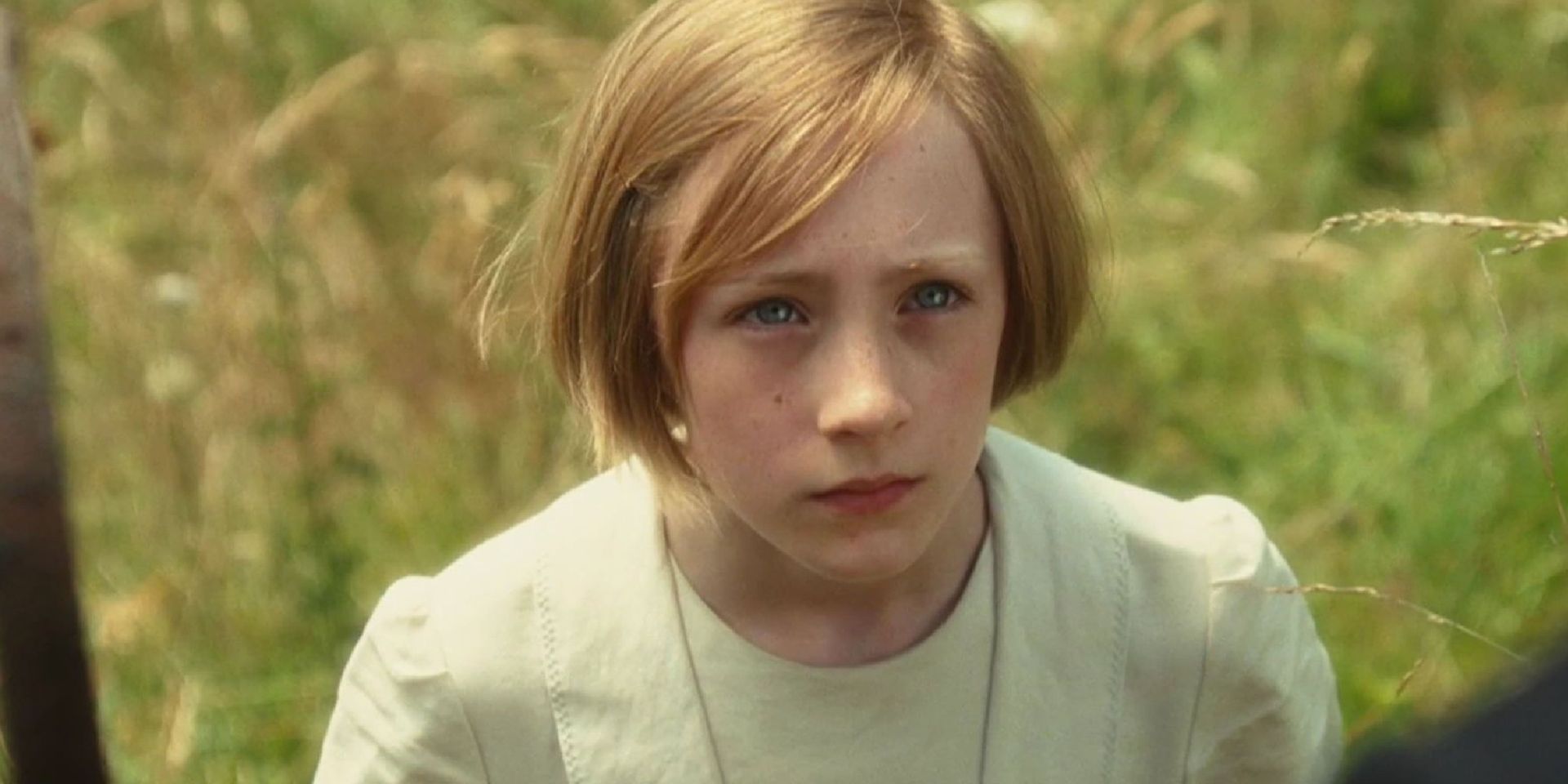 Young child with short blond hair in a light shirt, standing outdoors with a serious expression.