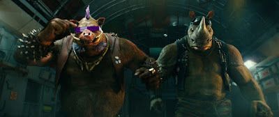 Two armored mutant turtles stride forward in a dark sewer tunnel, one wearing a purple mask.