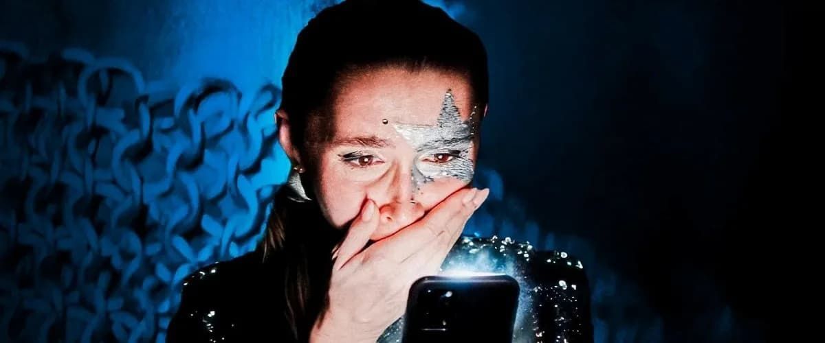Person with glittery face covering mouth, blue lighting, and abstract blue background