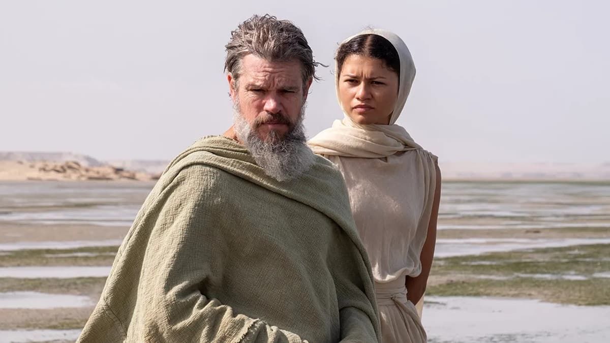 Two people in cloaks standing in a barren desert landscape under a pale sky