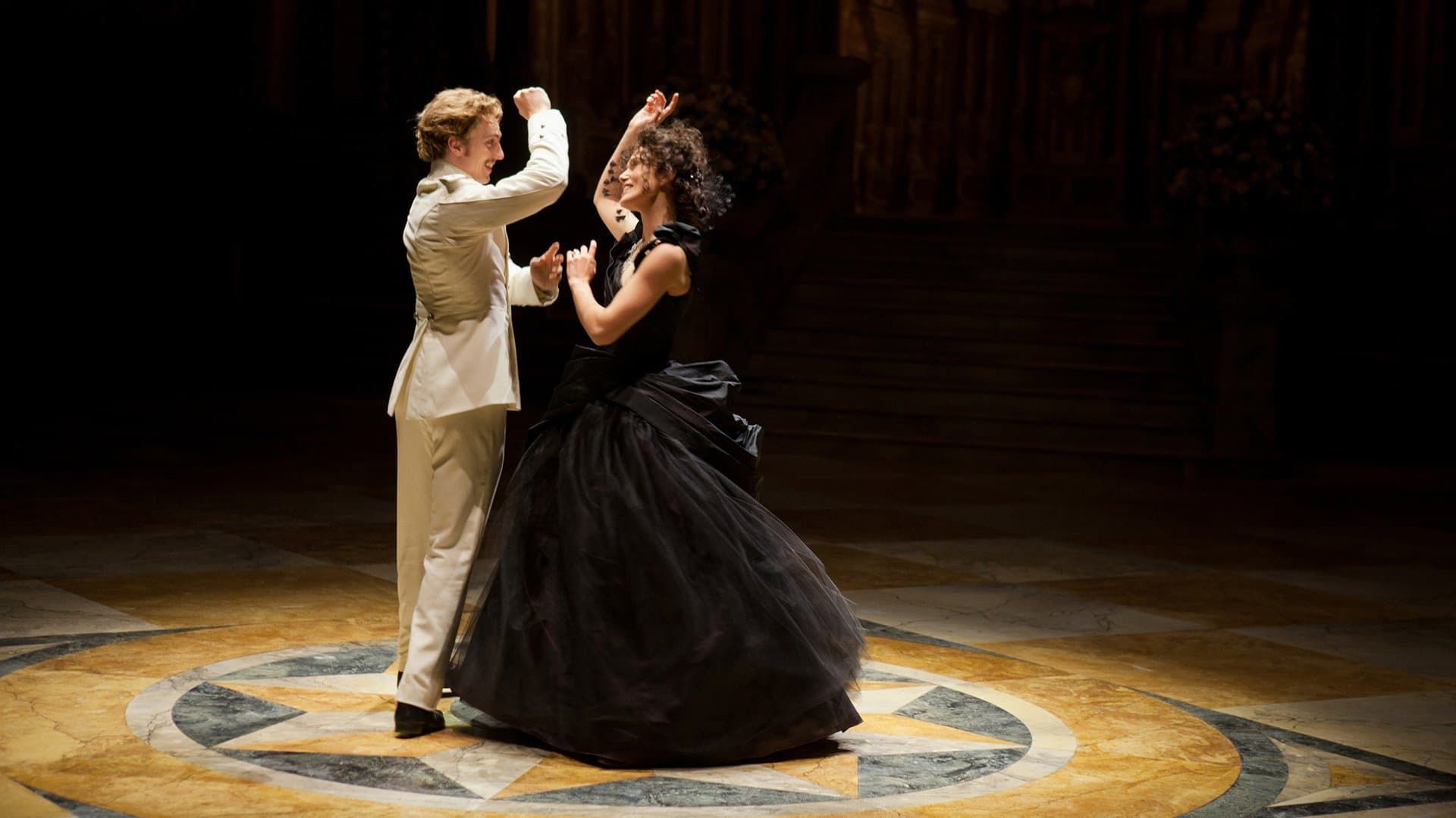 A couple dancing in formal attire on a spotlighted stage with a circular floor design.
