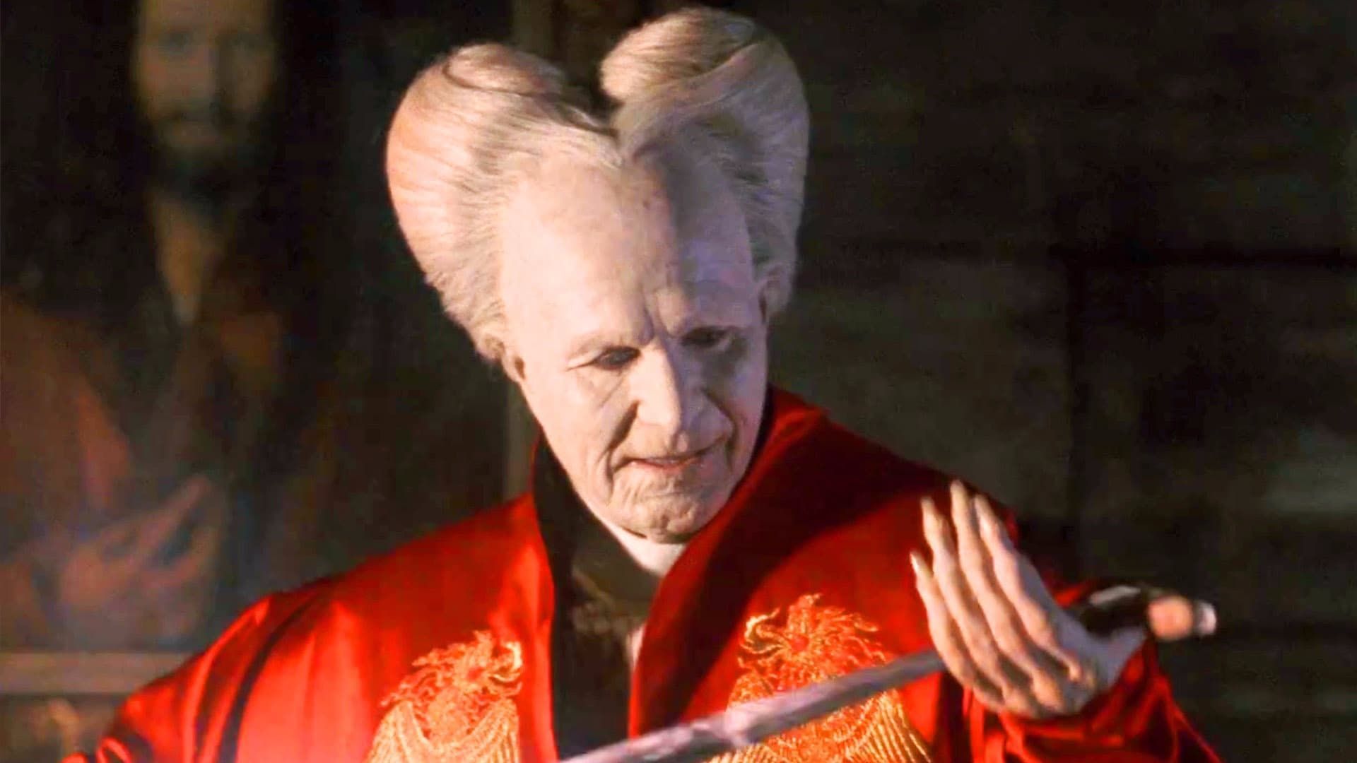 A person in a red robe with large pale horns gestures in a dimly lit room.