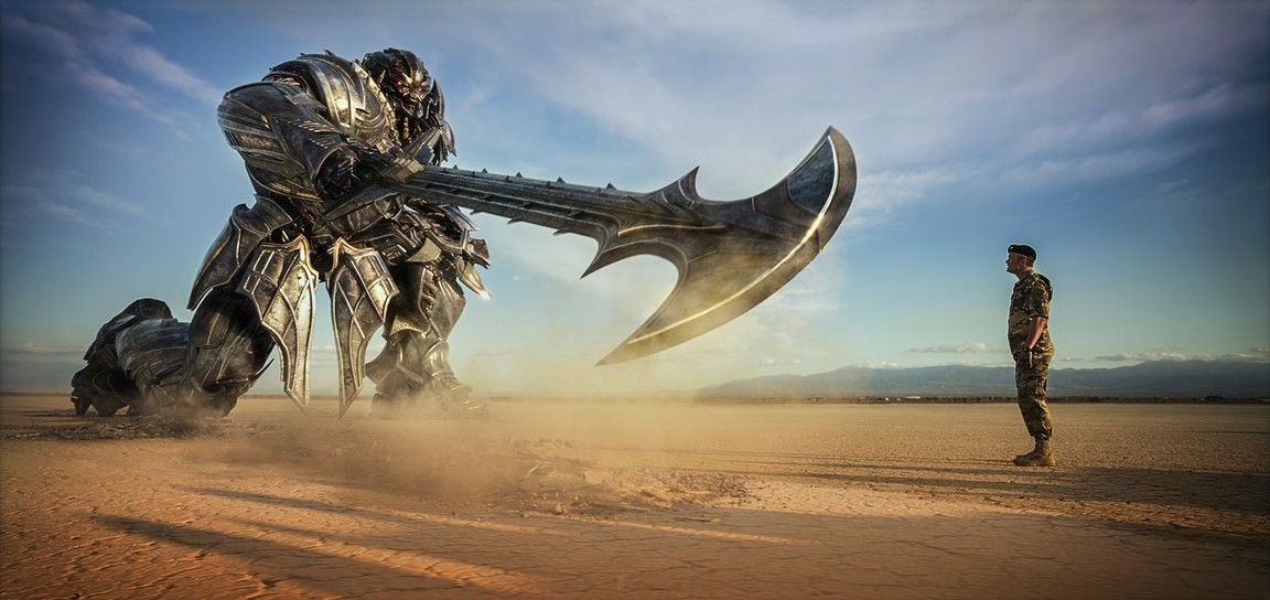 A large robot with a giant axe faces a soldier in the desert.