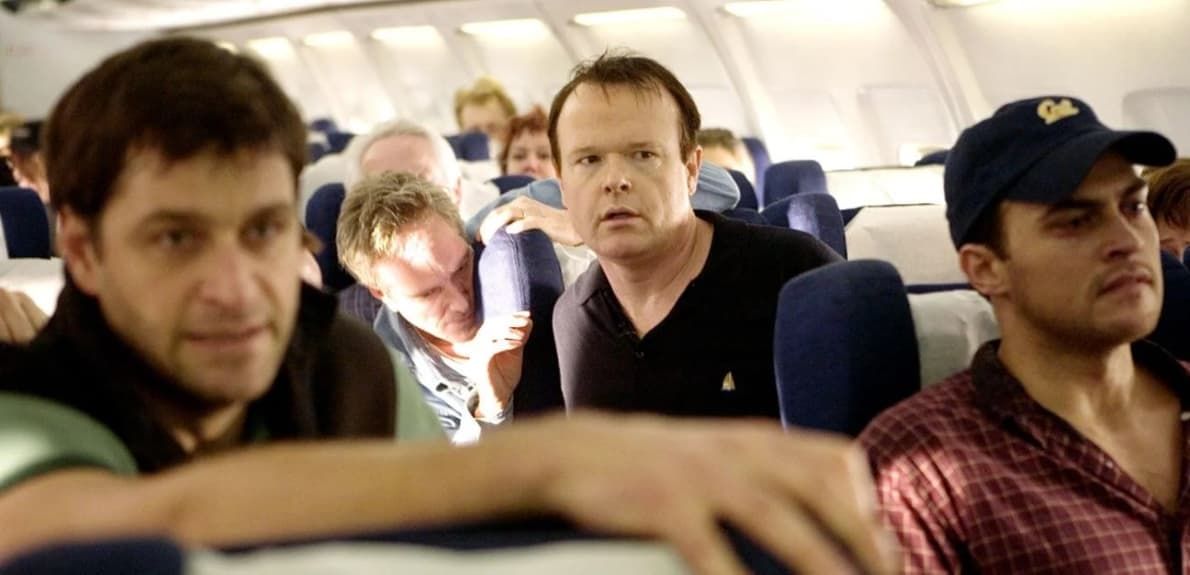 Several passengers seated inside an airplane cabin, with one man in a cap in the foreground
