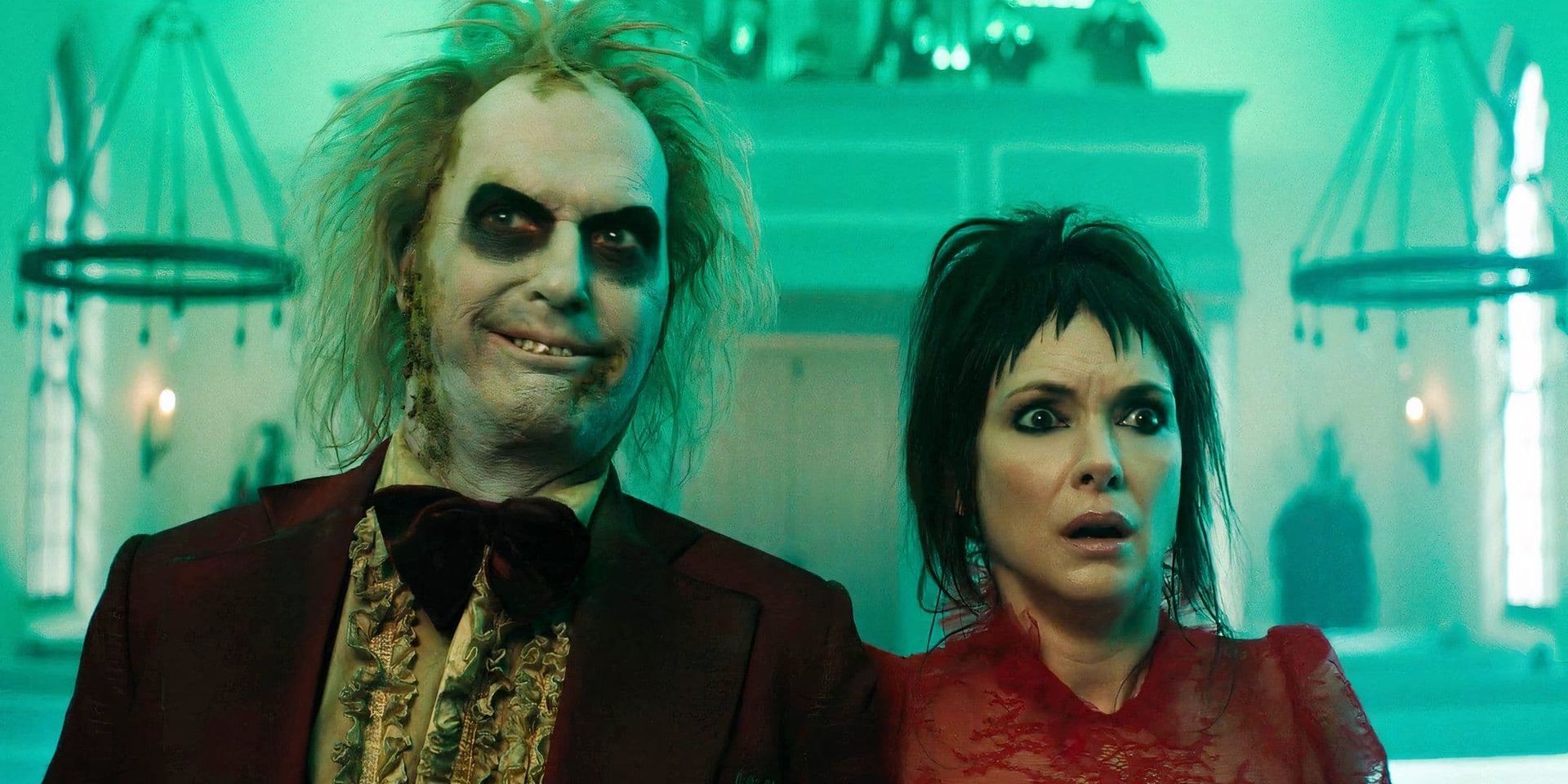 Grinning man in a burgundy suit stands beside a shocked woman in a dim, green-lit room