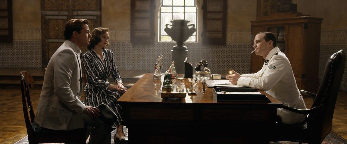 A couple sits across from a doctor in a bright room. The doctor gestures while speaking.