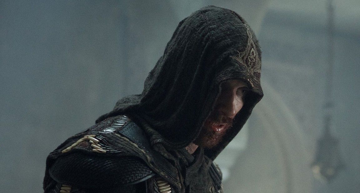 Man in assassin hood, looking down, wet and worn clothing, overcast setting.