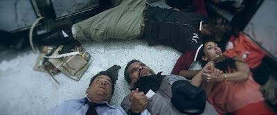 People lying on the floor, possibly injured. One man holds a gun. Dark setting.