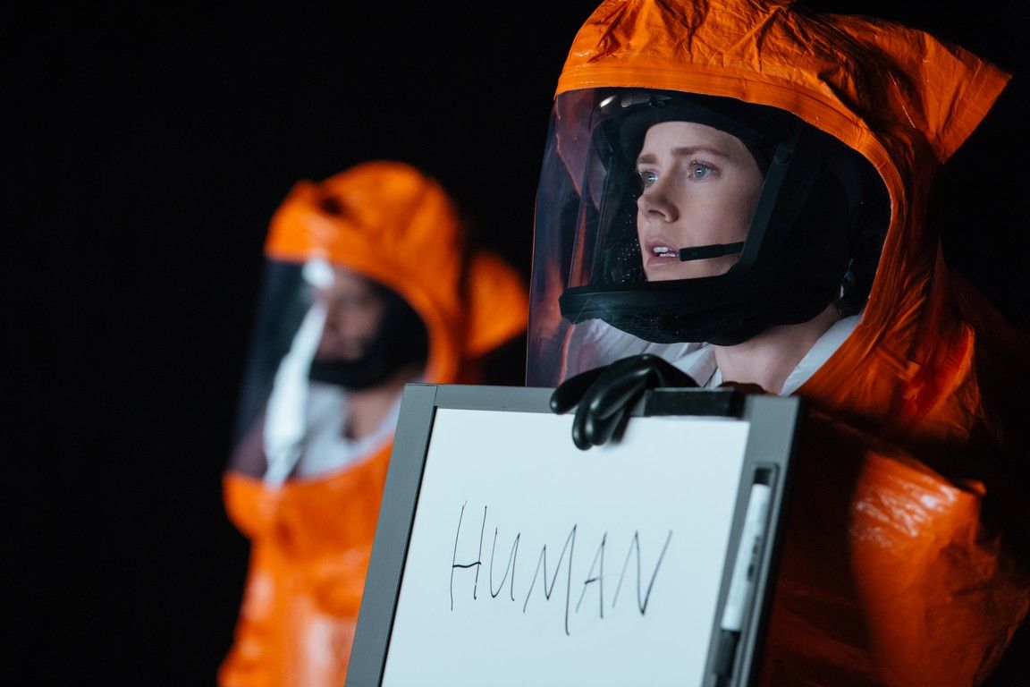 Two people in orange hazmat suits hold a sign that reads