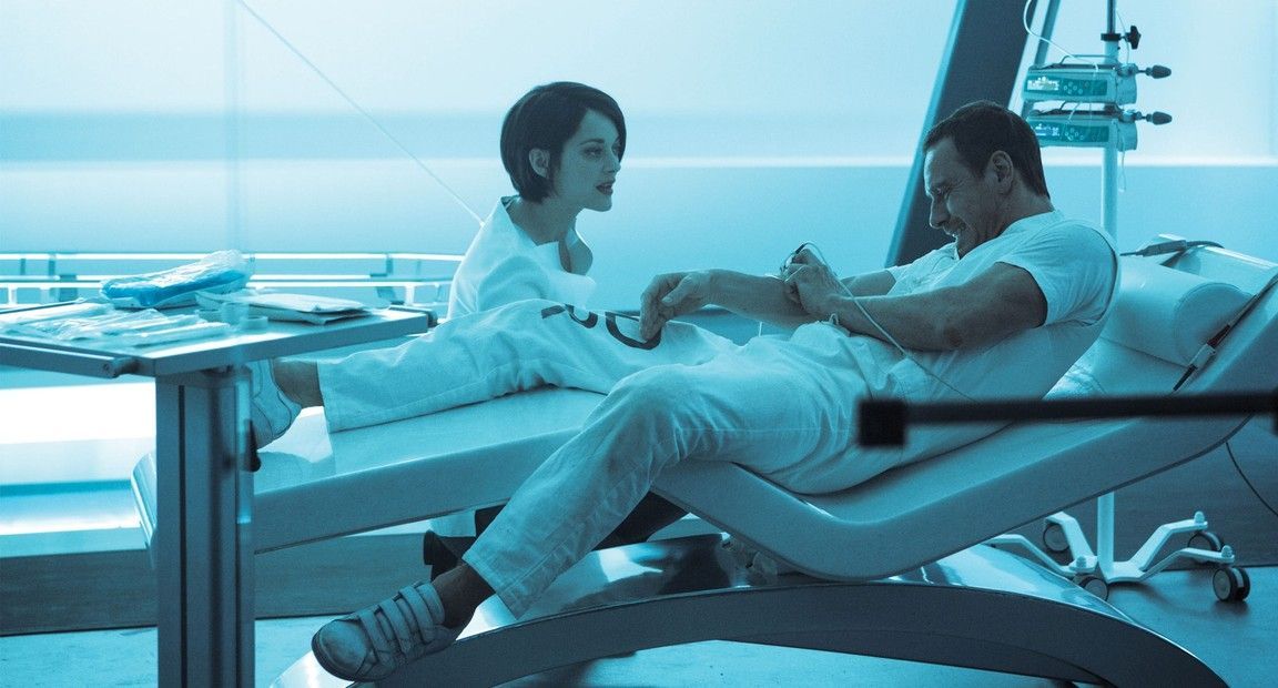 Man in white reclined, foot examined by a woman in white in a sterile, blue-lit room.