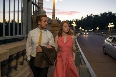 Couple walking along a bridge at dusk, with city lights and traffic in the background.