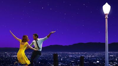 Two dancers in yellow and white pose by a lit lamppost under a purple night sky overlooking a cityscape