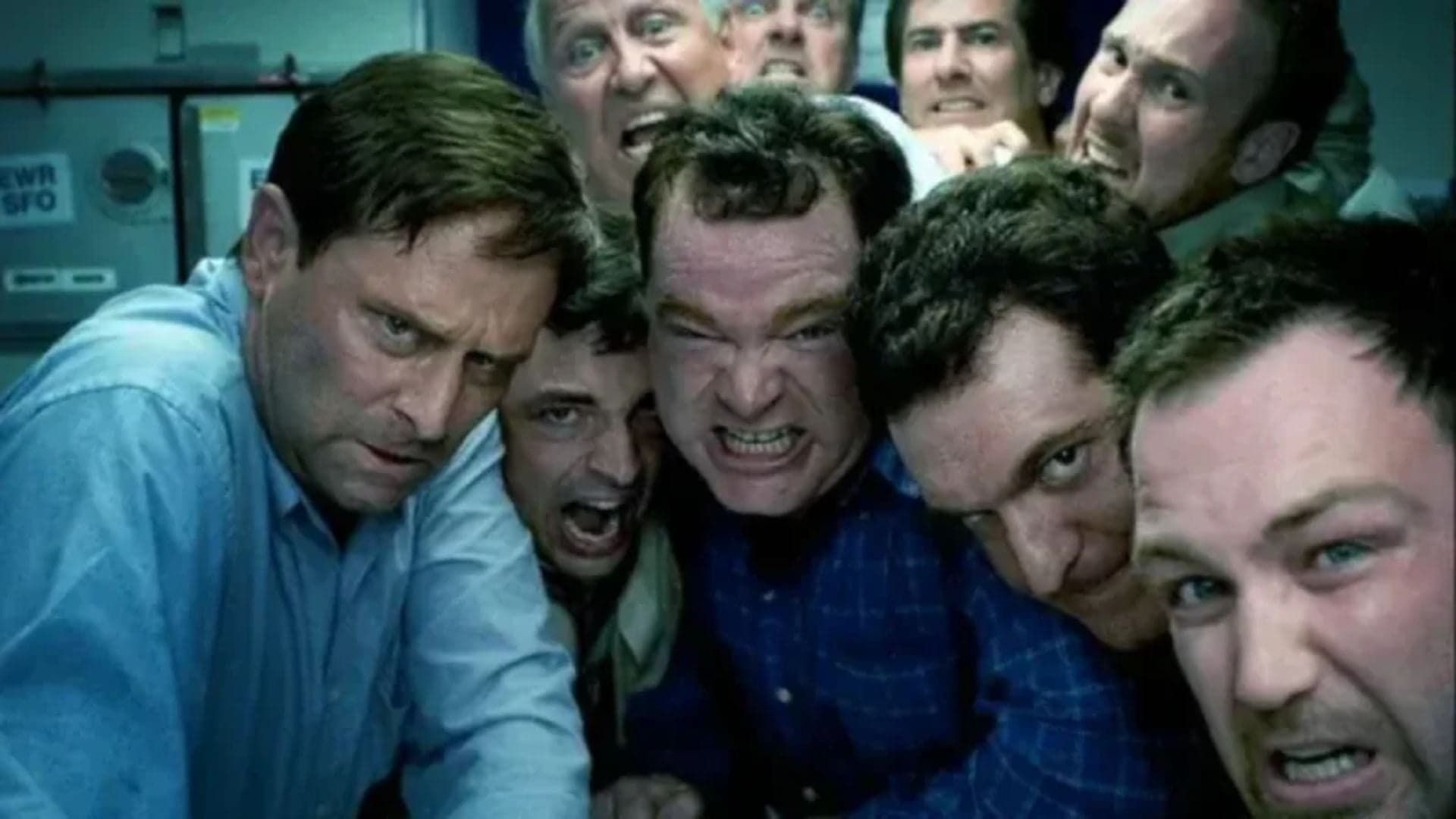 Several men crowded together in a cramped space, grimacing and making tense faces.