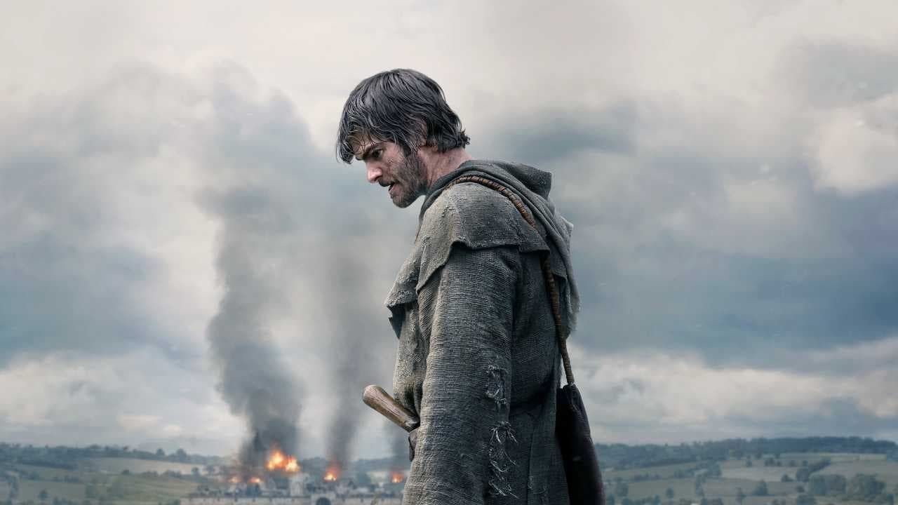 A cloaked figure stands before a smoky battlefield under a gray sky.