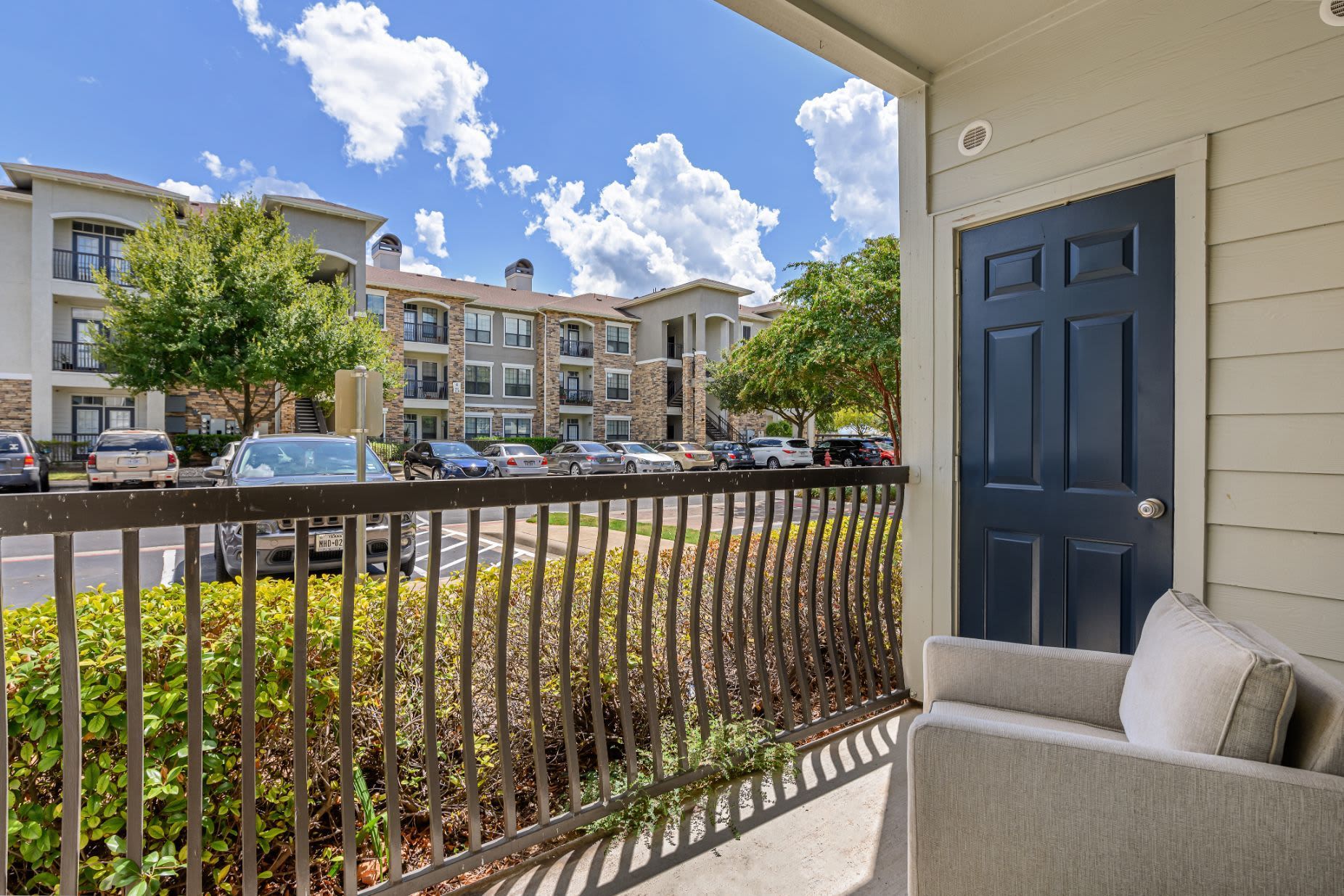 A balcony with a chair and a black door with a building in the background at Marquis Lakeline Station in Austin, TX.