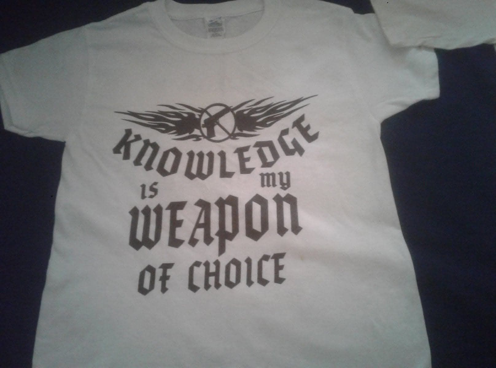 White T-shirt with black text reading “Knowledge is my weapon of choice” and a winged graphic