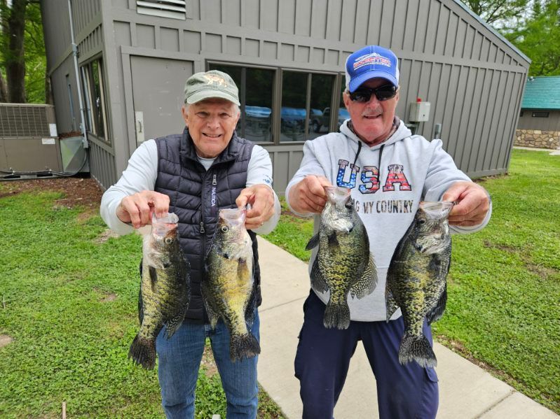 Two people holding up large fish in front of a house on a grassy lawn.