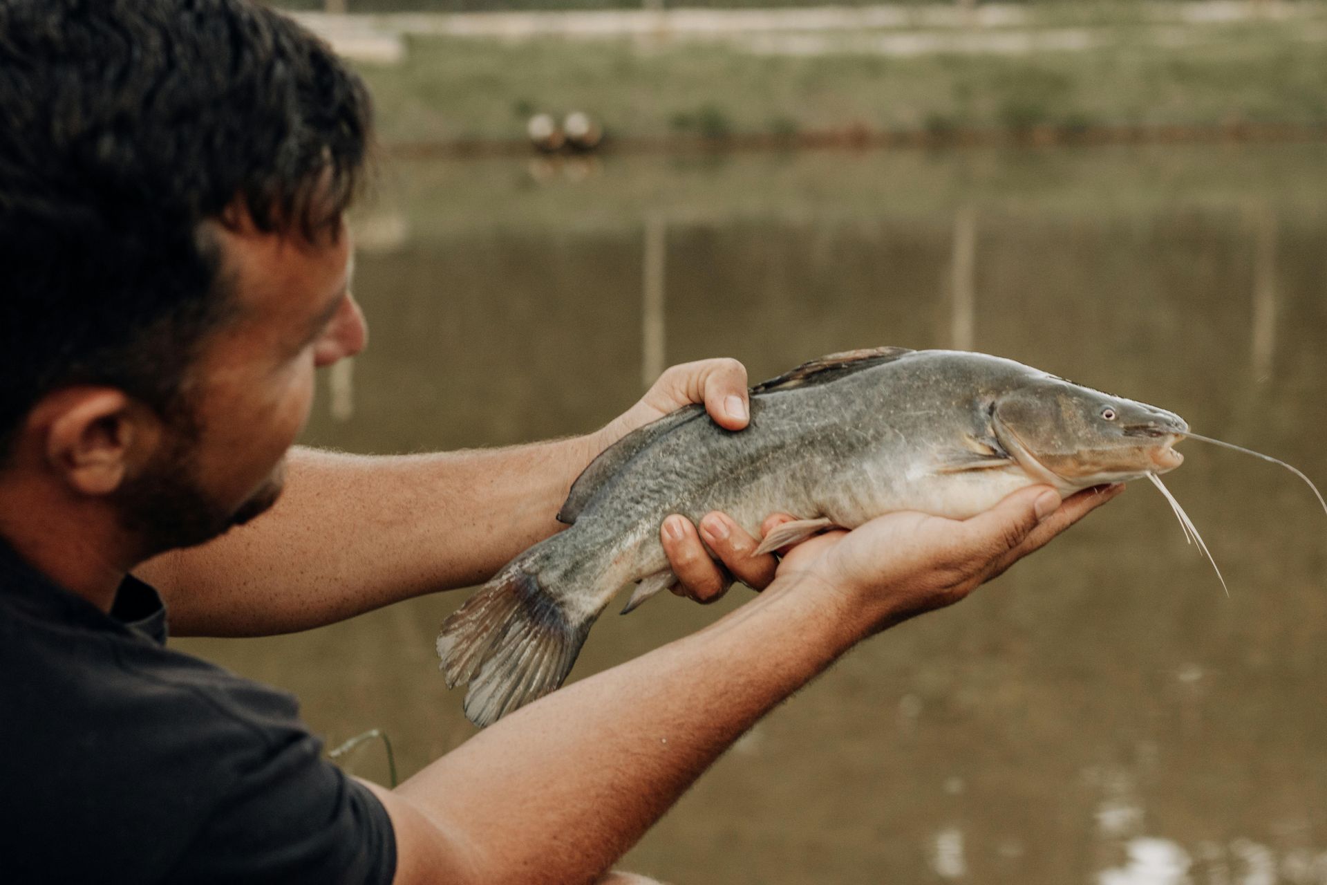 Person holding a large fish over a muddy riverbank