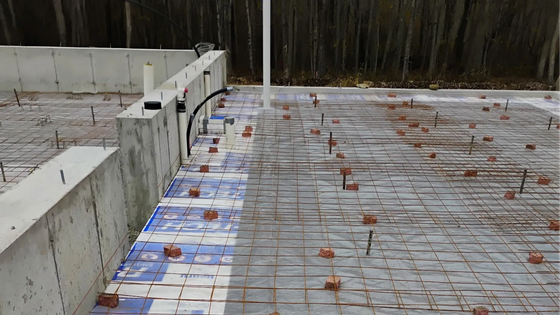 Concrete foundation slab with steel rebar grid and blue waterproofing along the edge at a construction site