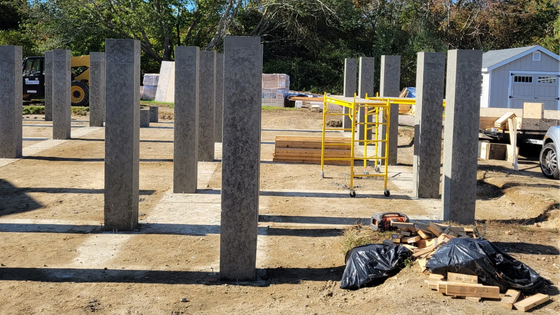 Concrete columns rising from a construction site with yellow scaffolding and equipment on dirt ground.