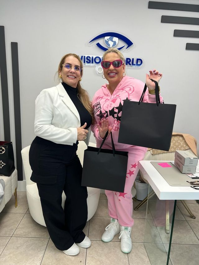 Two women are standing next to each other in a room holding shopping bags.