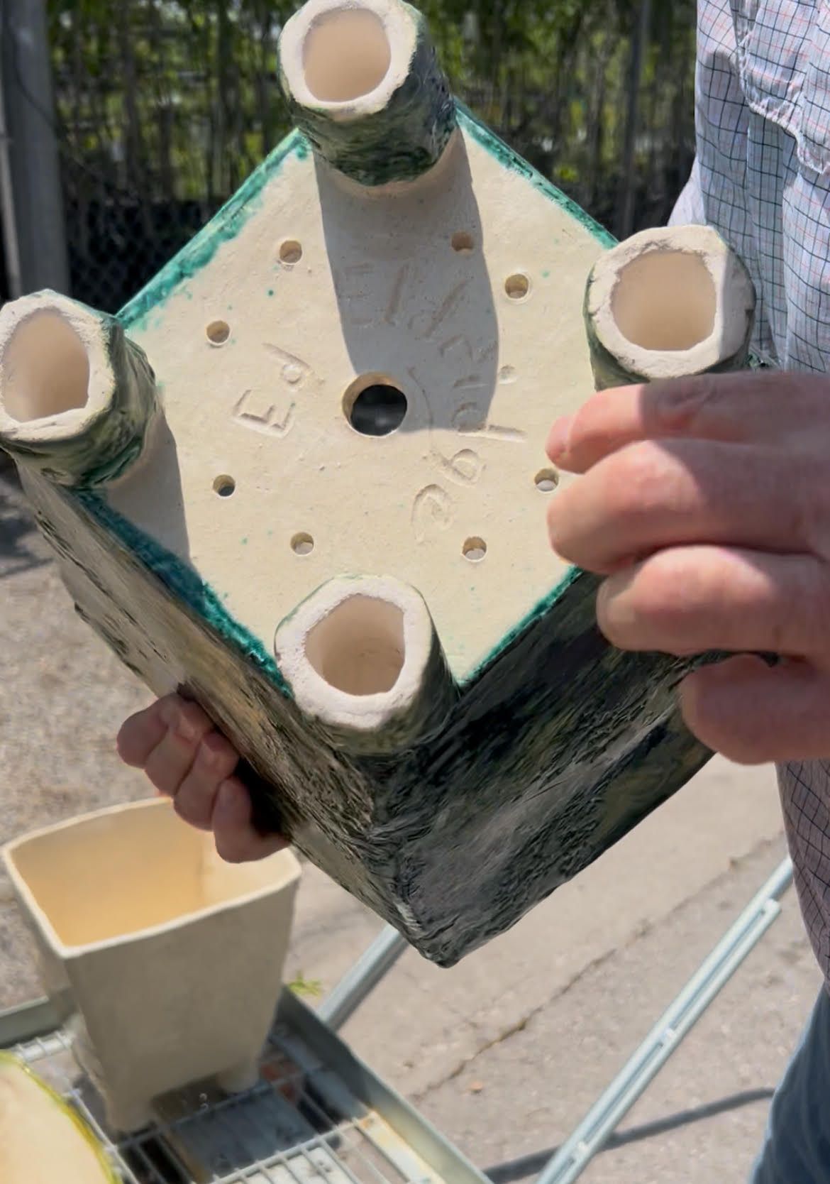 Hands holding a square mold filled with concrete around four white PVC pipe openings