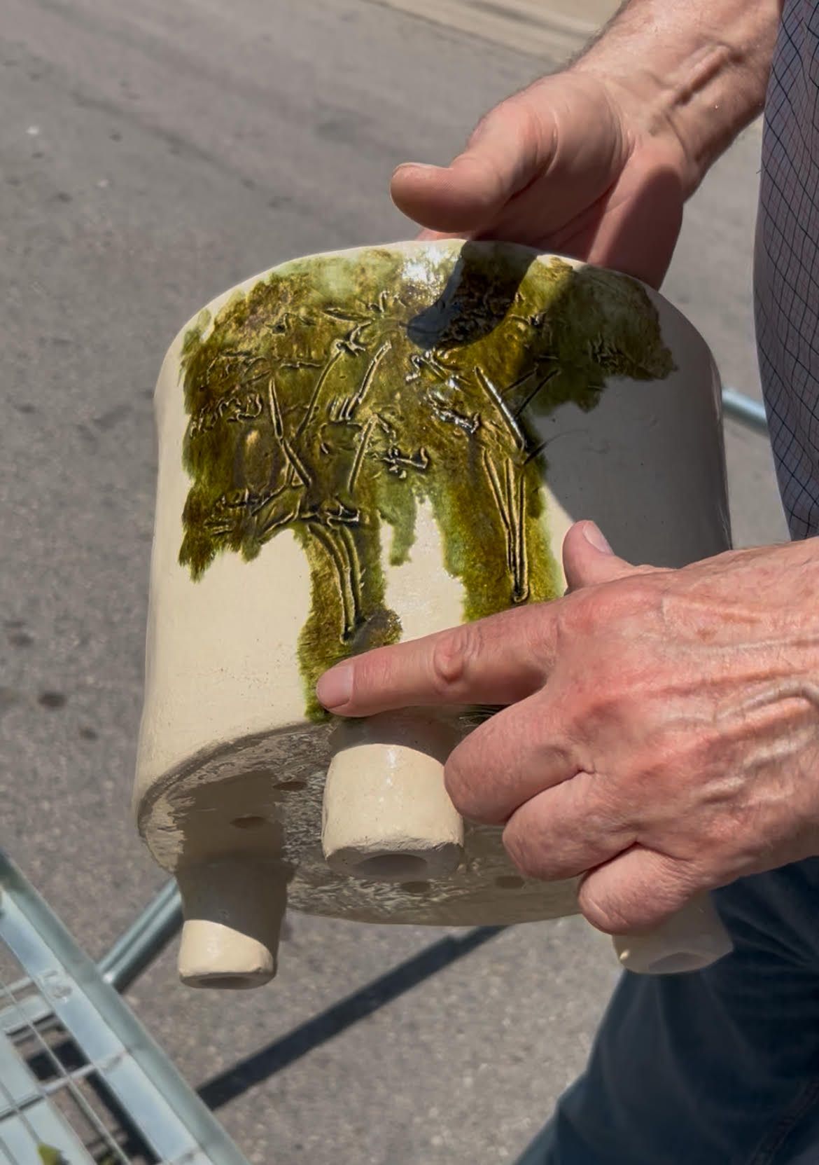 Hands holding a moss-covered ceramic pipe fitting outdoors on pavement