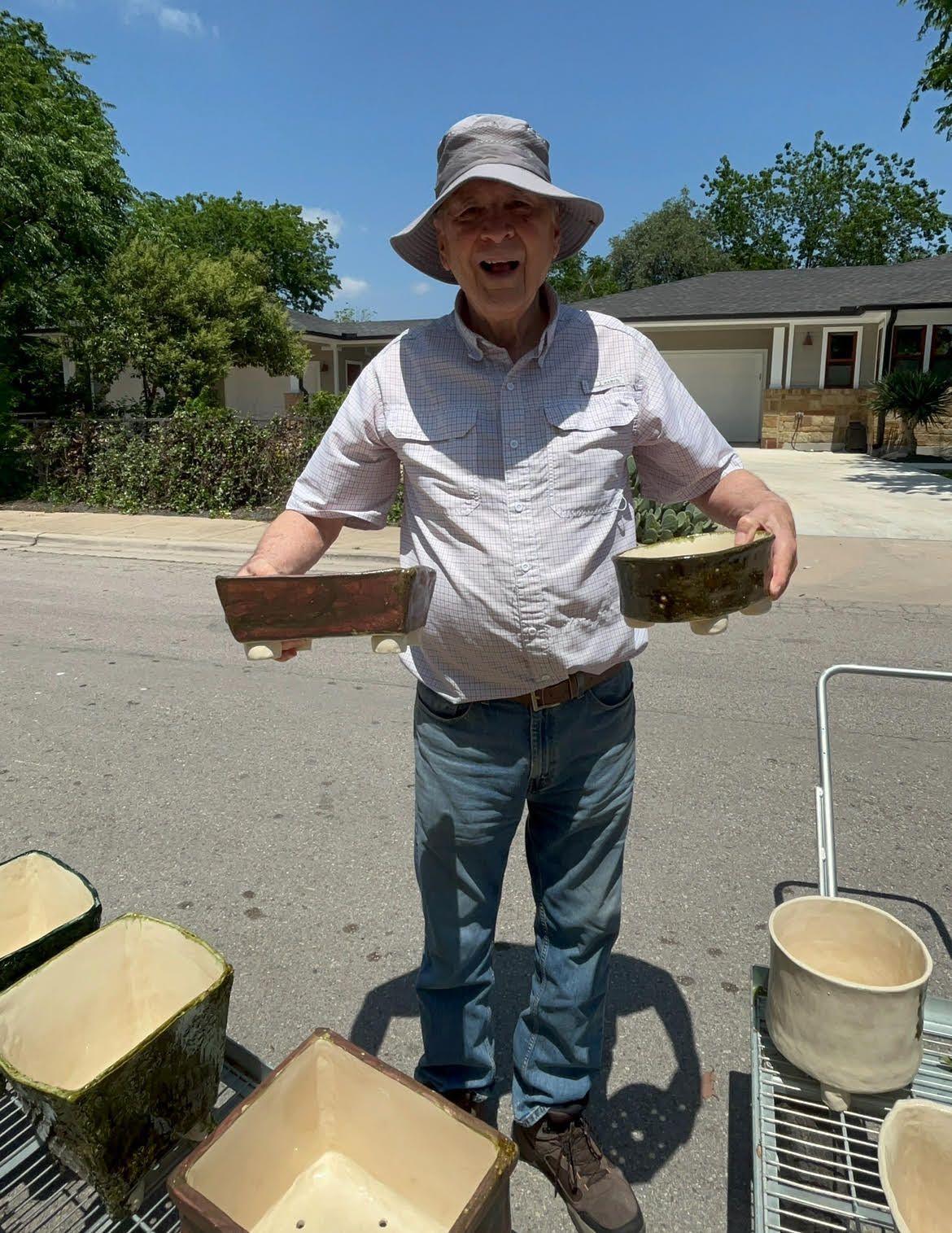Person outdoors holding trays, standing near buckets and plants in a sunny yard
