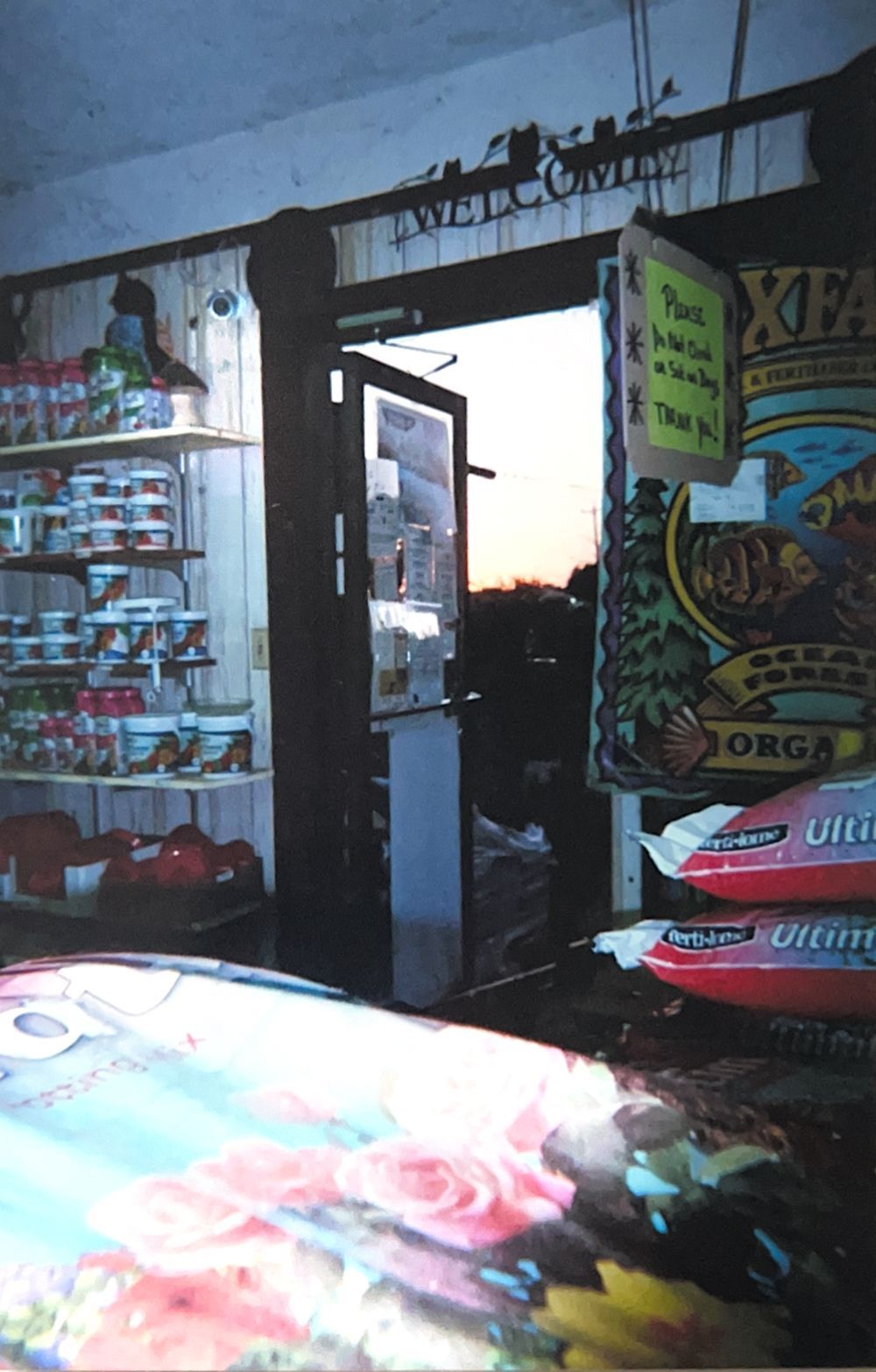 Small shop interior with open doorway at sunset, shelves of goods, and colorful products in the foreground