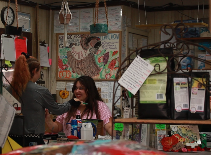 Two women behind a colorful shop counter with hanging items and shelves of goods