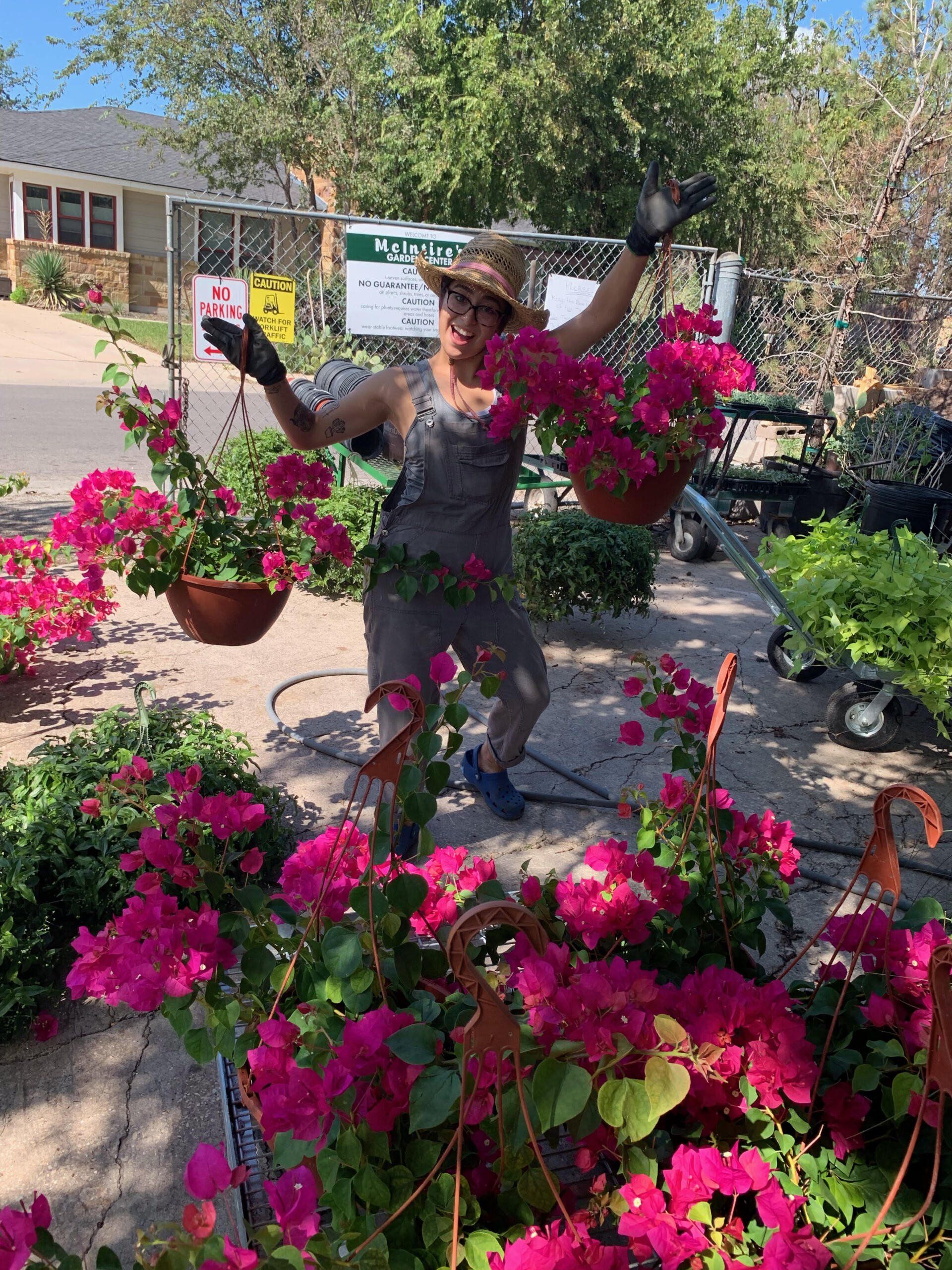 Person posing among bright pink flowers in a sunny garden courtyard