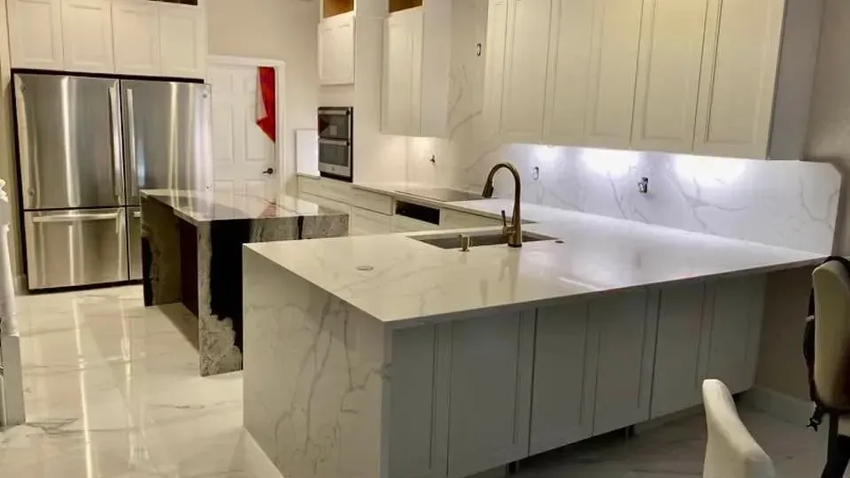 Modern white kitchen with island, stainless steel fridge, and glossy tile floor