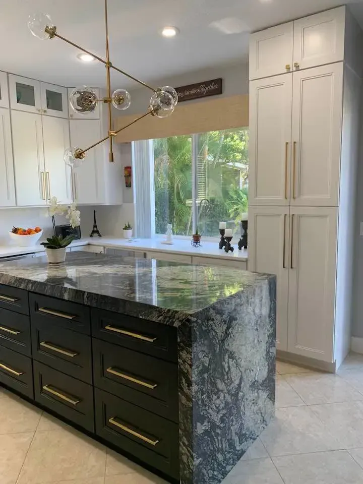 Modern kitchen with dark island, granite countertop, white cabinets, and a large window overlooking greenery