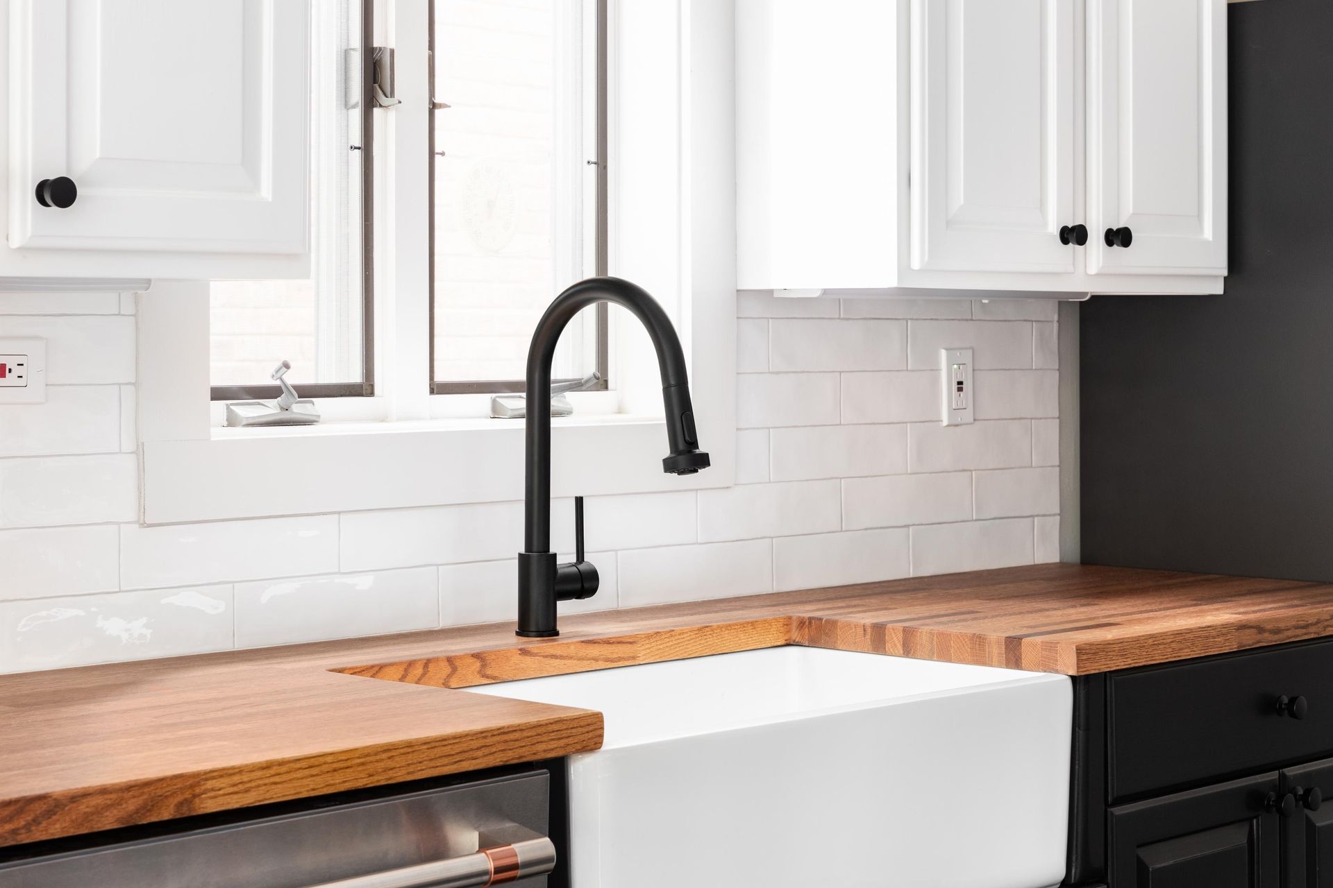 Modern kitchen with white cabinets, wood countertops, black faucet, and white apron-front sink