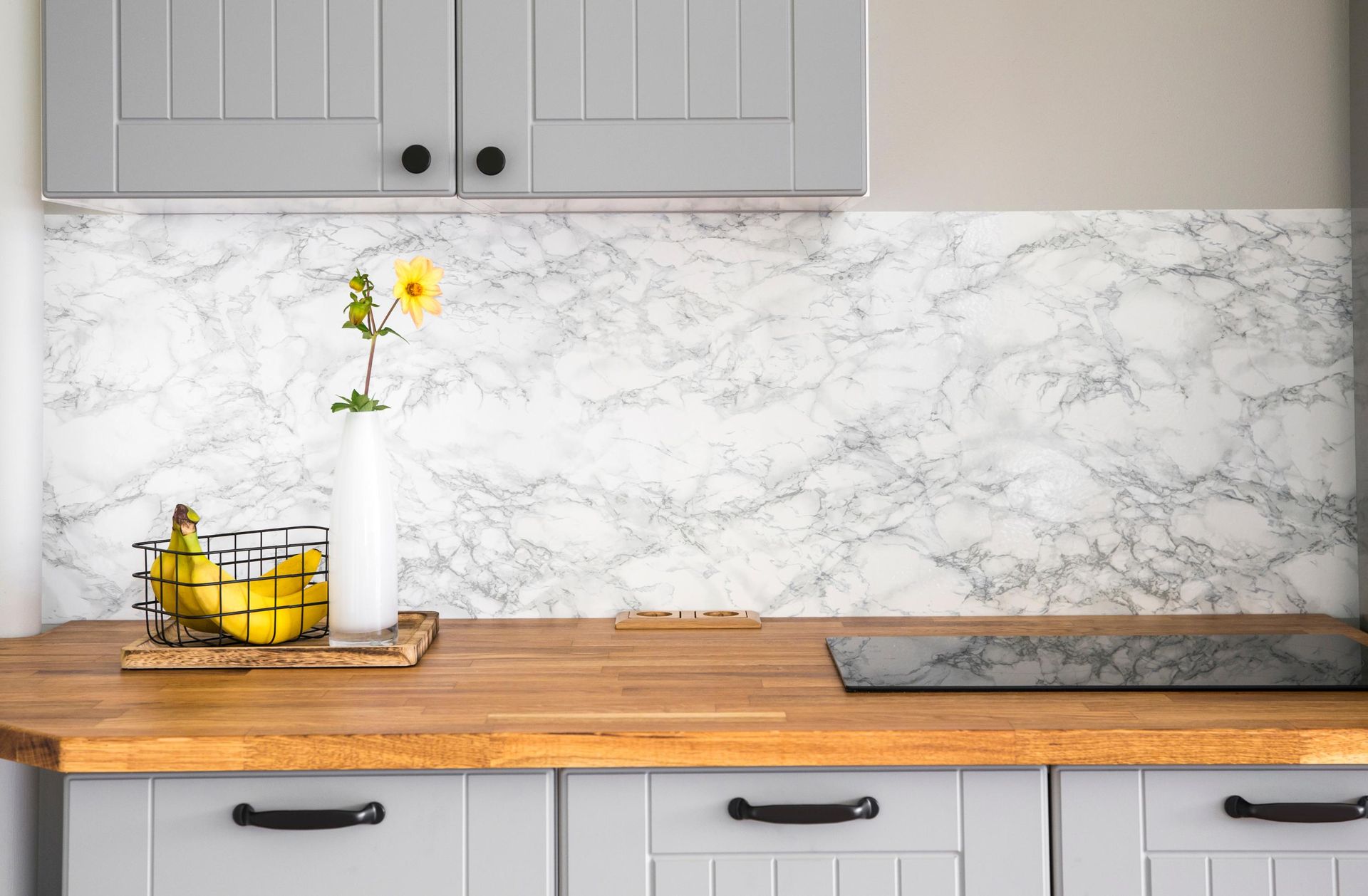 Modern kitchen countertop with gray cabinets, marble backsplash, and a vase, basket, and lemon decor