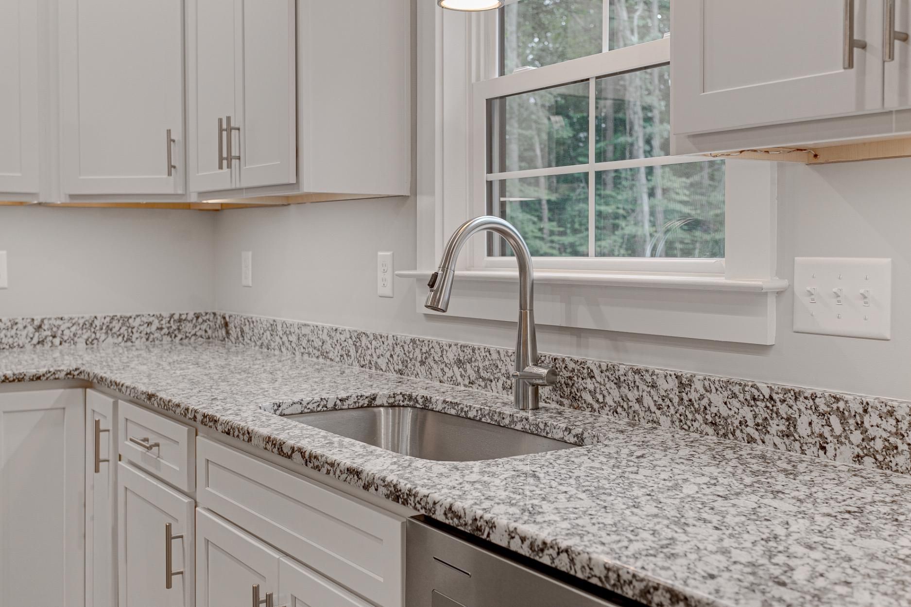 Bright kitchen with speckled granite countertop, stainless sink, and window above it