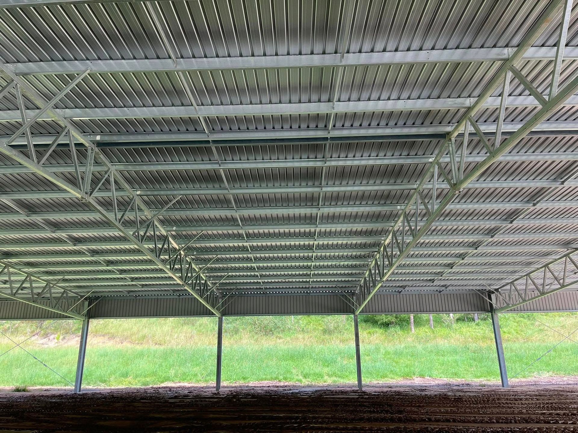 Underneath view of a metal-framed roof structure, supported by columns. Wooden slats cover the frame, with green grass in the background. — Equine Stable Solutions In Diddillibah, QLD