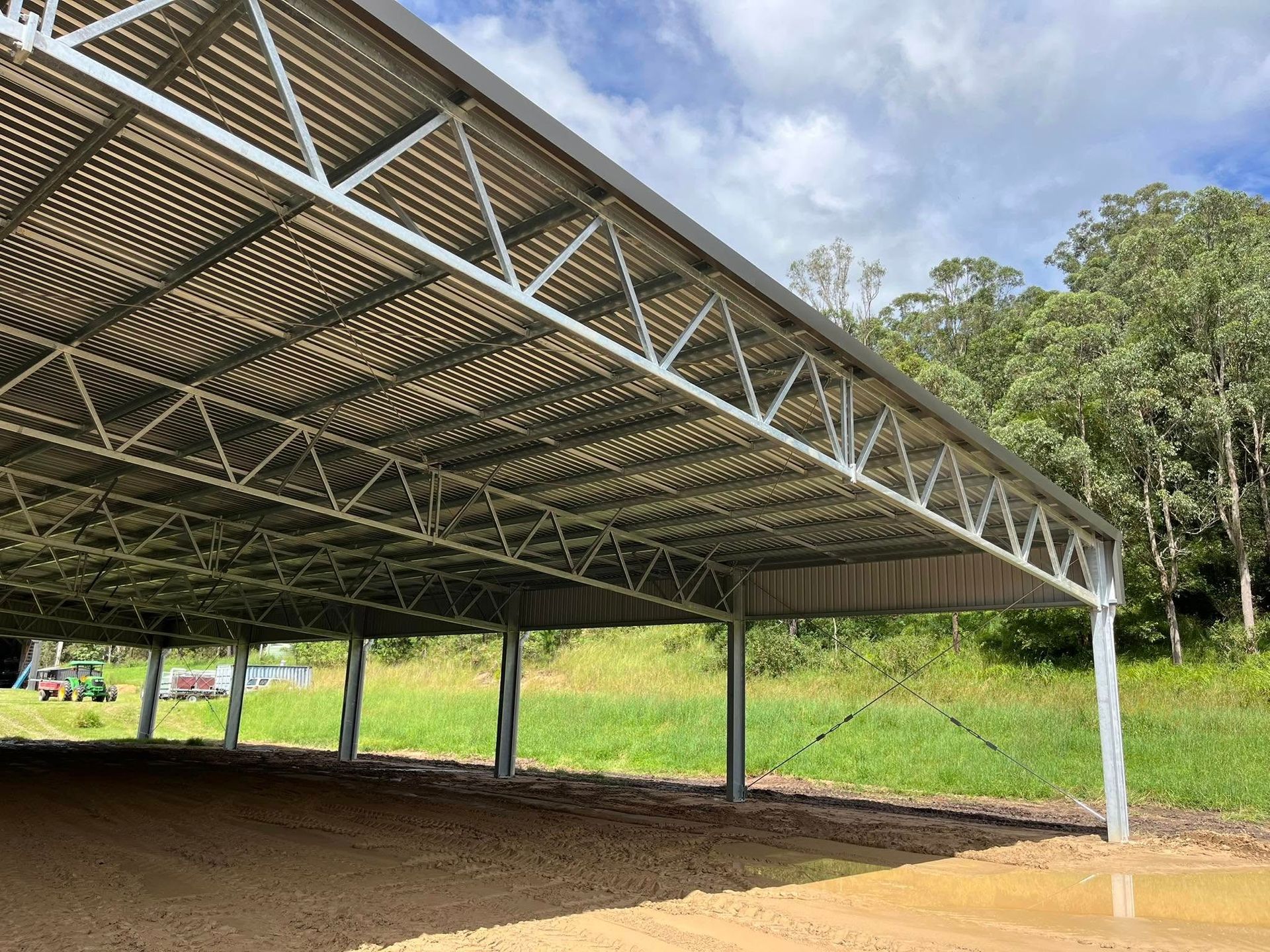 Steel-framed shelter with a corrugated roof, over a dirt area, in a grassy field with trees. — Equine Stable Solutions In Diddillibah, QLD