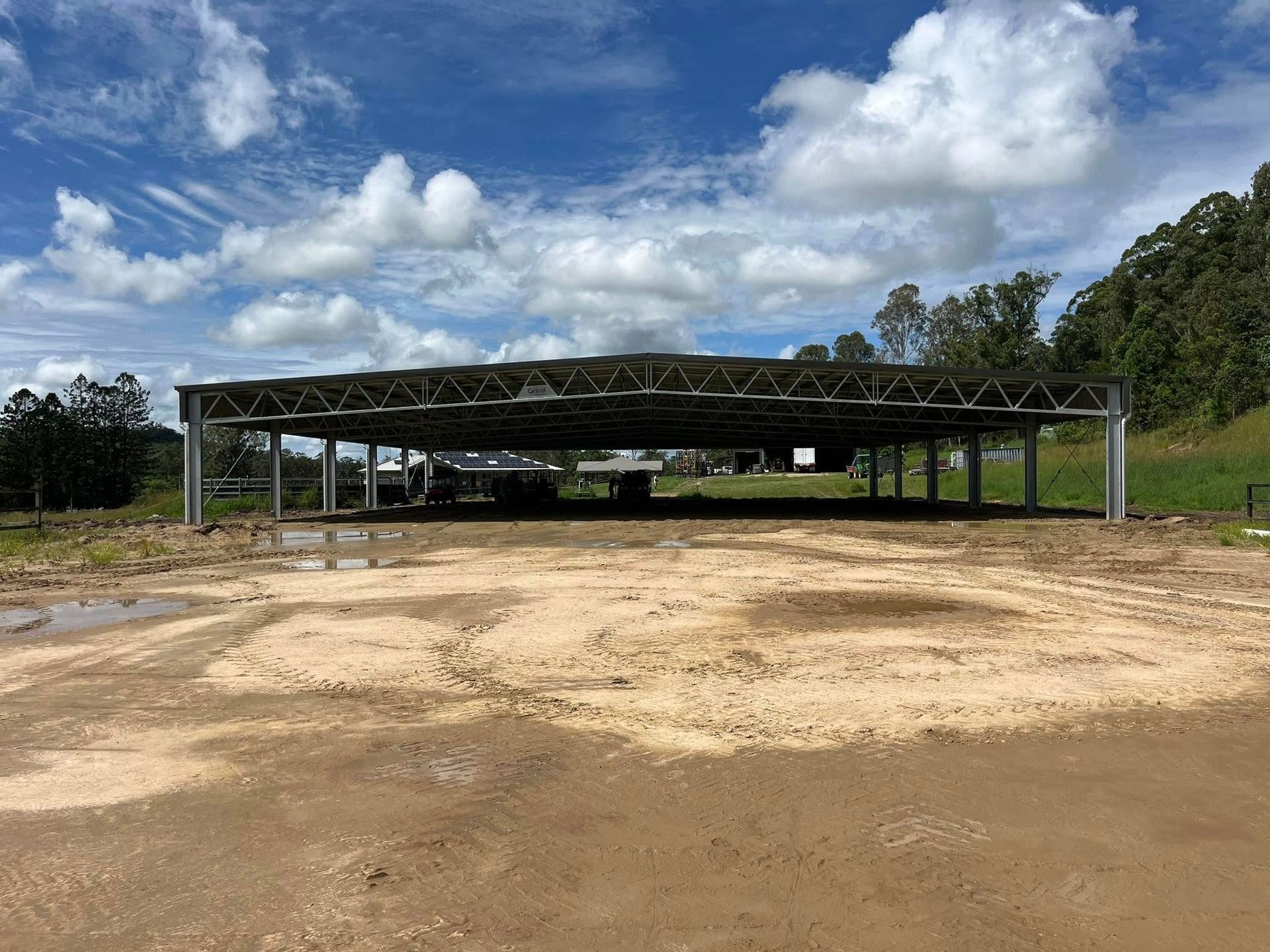Metal-framed open-sided shed in a dirt lot under a cloudy blue sky. Trees in background. — Equine Stable Solutions In Diddillibah, QLD