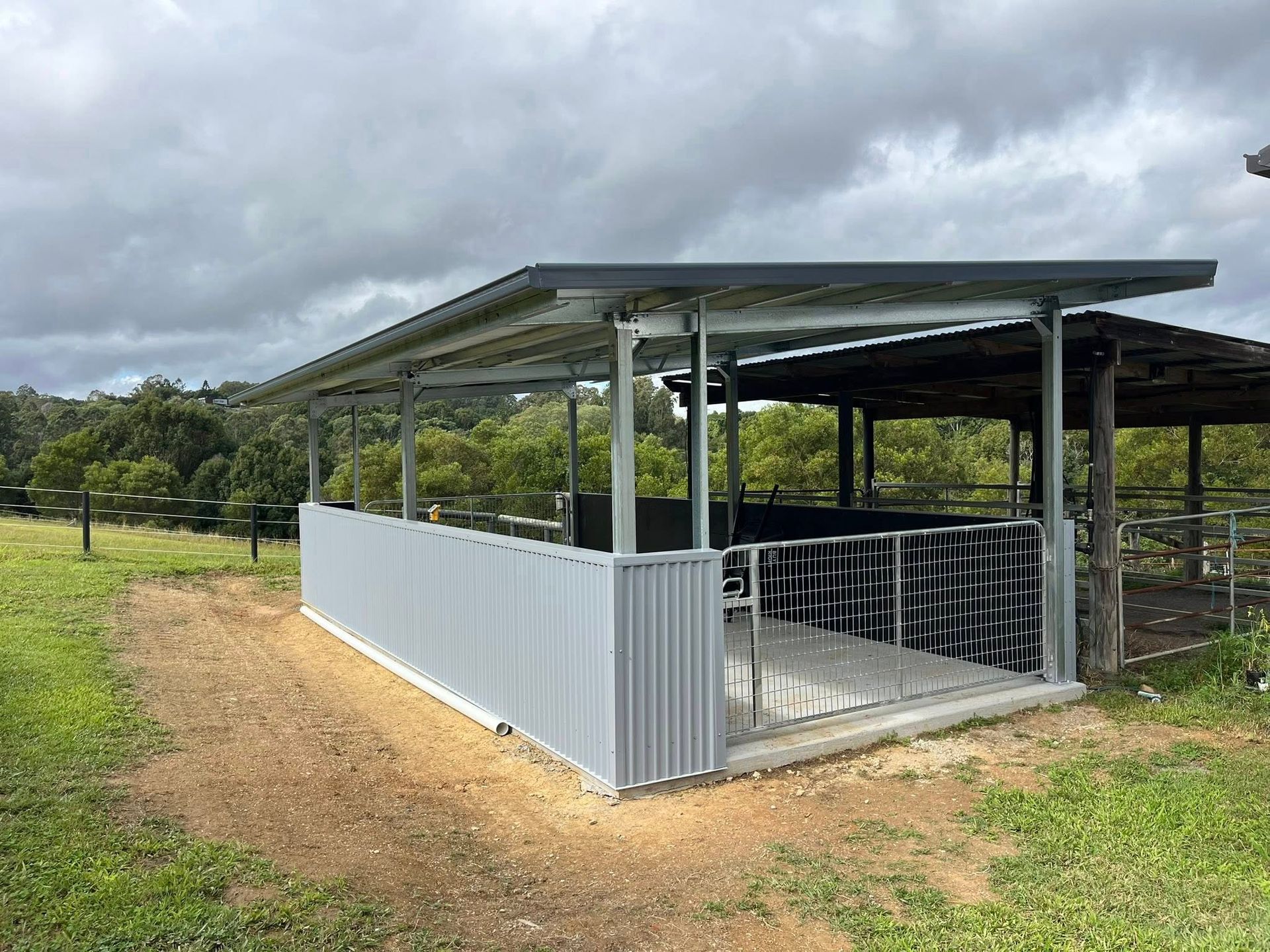 Outdoor metal shed with corrugated walls and roof, set on dirt ground. Green grass and trees in background. — Equine Stable Solutions In Diddillibah, QLD