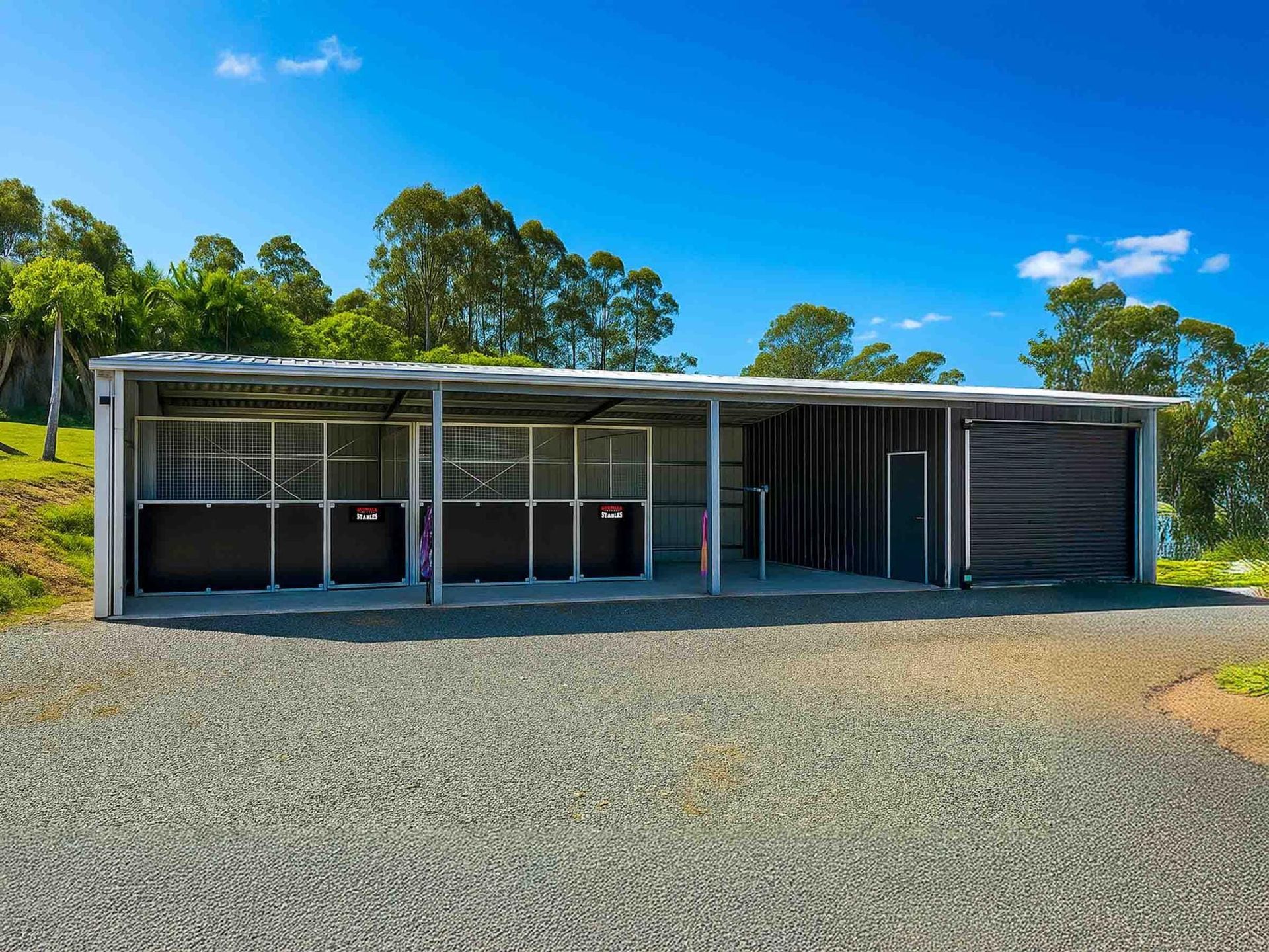 A Large Gray Building With A Black Fence Around It — Equine Stable Solutions In Diddillibah, QLD